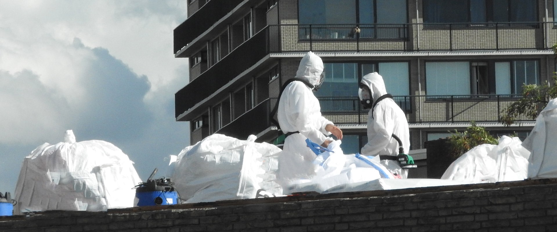 Two Asbestos removal technicians wearing personal protective equipment (PPE) and bagging up asbestos on a commericial site.