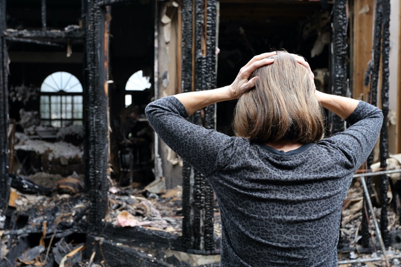 The woman holding hands on her head in despair looking at her fire-damaged home.